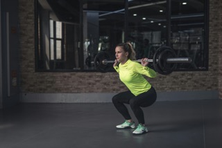 Woman performing a barbell back squat in a gym with a shoulder-width stance