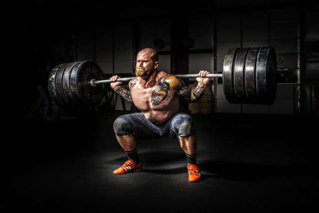 Male powerlifter performing deep barbell back squat with proper form and heavy weight